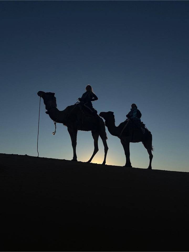 Silhouette of two riders on camels against a dusky sky with the sun behind them