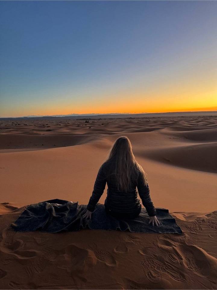 Traveler gazes over rippling desert dunes bathed in the last light of day