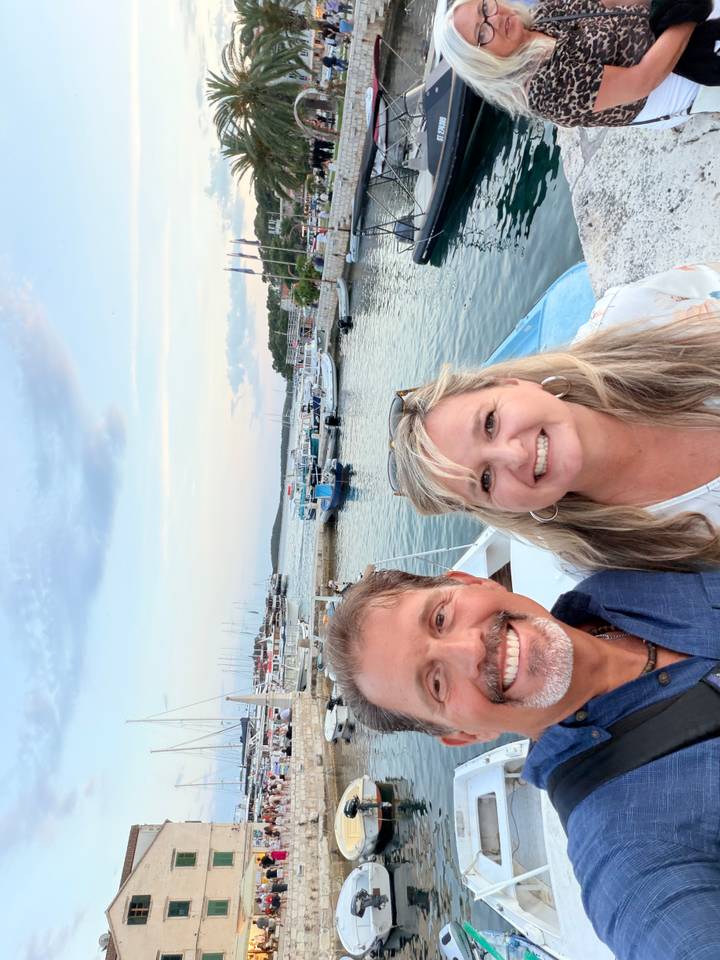 Couple selfie at a marina with boats and soft evening light in the background.