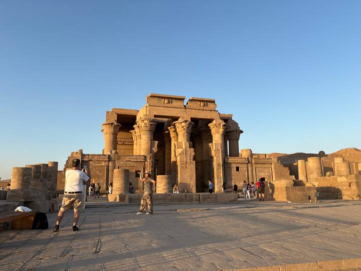 Kom Ombo Temple bathed in warm evening light with tourists exploring the forecourt.