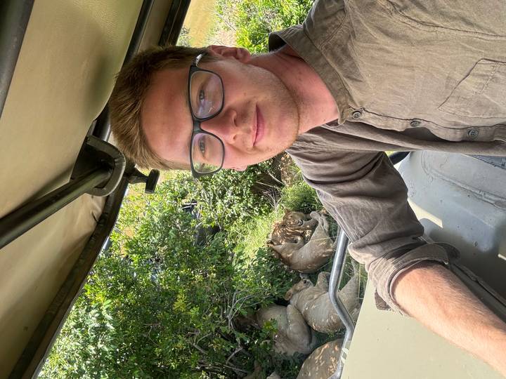 Safari tourist in a 4x4 smiles with a pride of resting lions visible through the vehicle window.