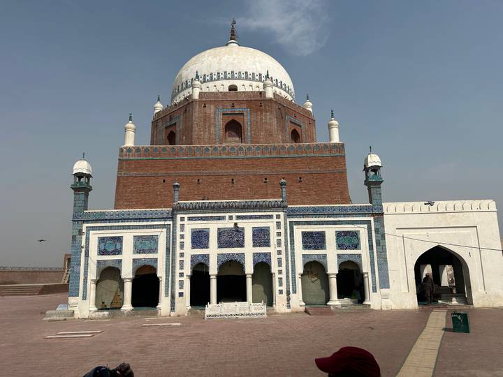 Impressive brick and blue-tiled mausoleum with a large white dome and minarets set against a pale sky.