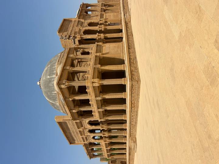 Historic sandstone palace with domed roof and intricate columns set beneath a cloudless blue sky.