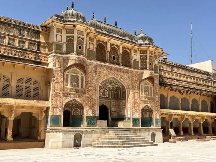 Intricately decorated gateway and courtyard of Amber Fort under clear sky.