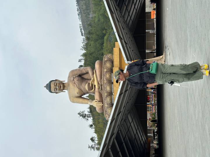 Tourist poses beneath the massive seated Buddha Dordenma statue in Thimphu, Bhutan.