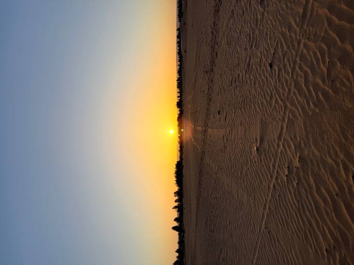 Orange sun setting over flat desert sands leaving rippled patterns in the foreground
