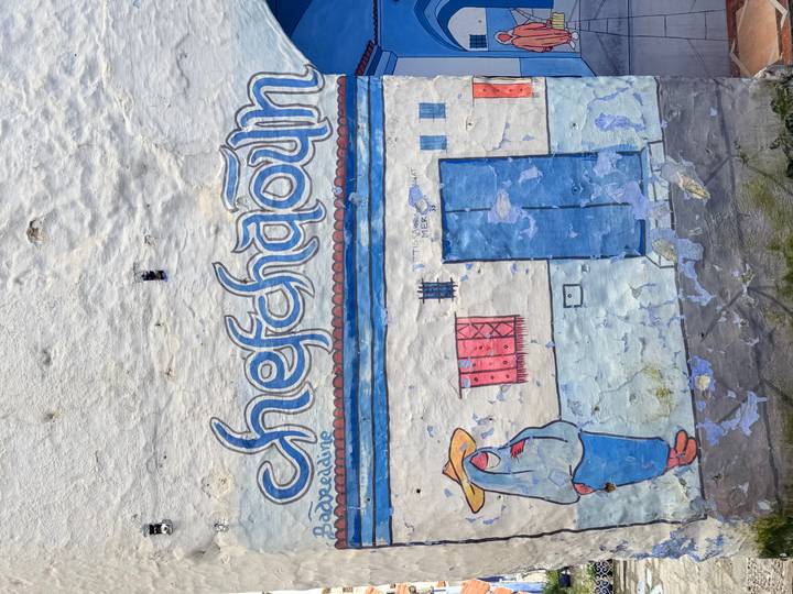 Painted wall mural reading 'Chefchaouen' with stylised figures and peeling blue plaster
