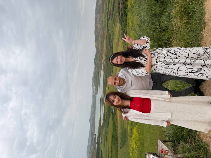 Three friends posing in front of rolling green countryside and a distant lake under cloudy skies