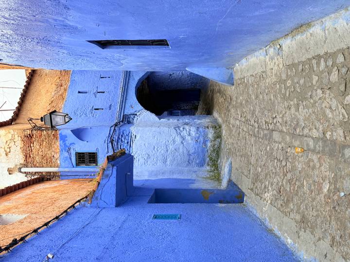 Quiet blue alleyway in Chefchaouen with arched doorway, lantern and cobblestone path
