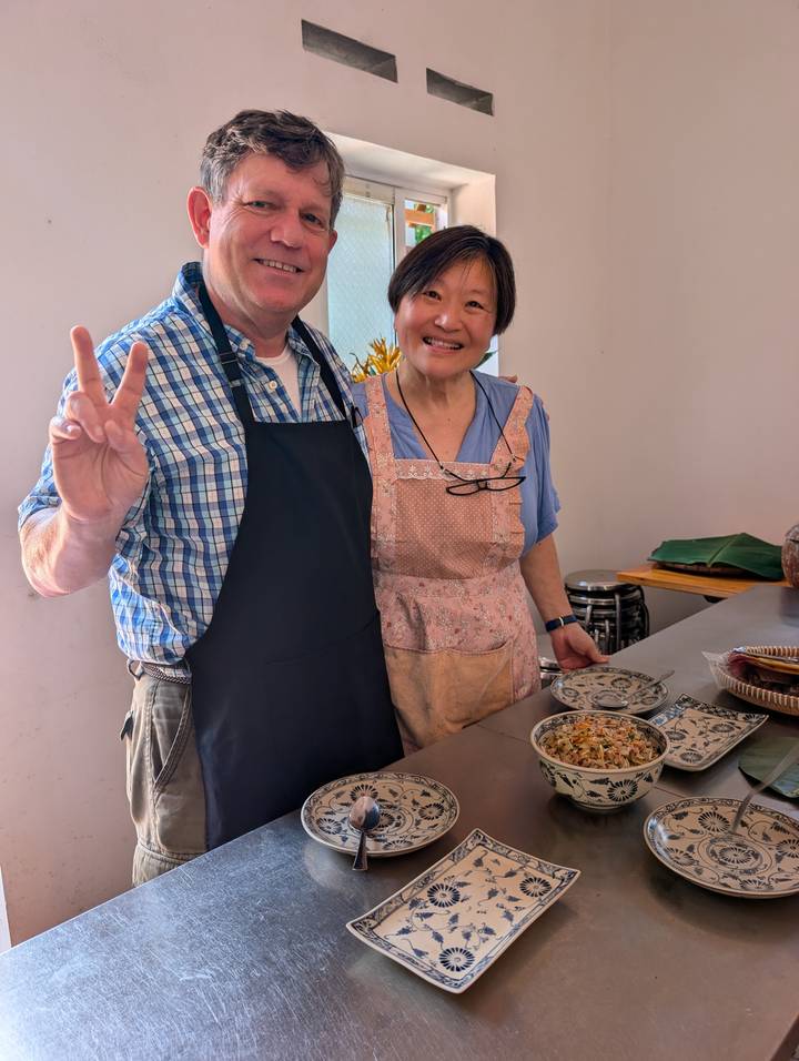 A smiling couple in aprons present a freshly prepared Vietnamese dish during a cooking class.