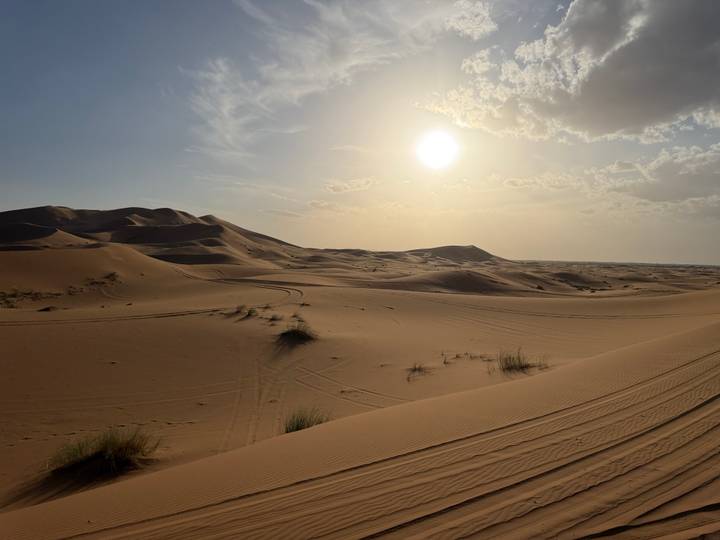 Vast golden dunes of the Sahara under a bright afternoon sun with soft clouds above.