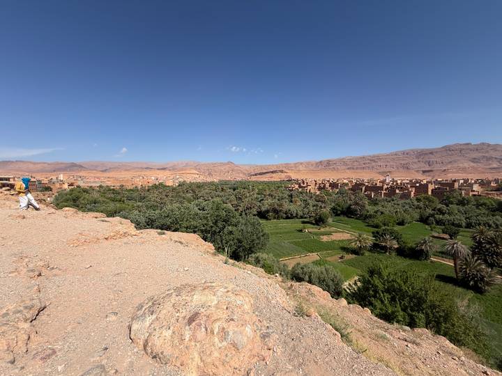 Panoramic view over a lush oasis valley with adobe village and mountains beyond.