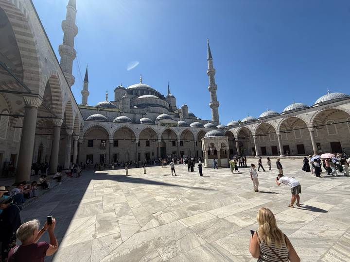 Courtyard of Istanbul’s Blue Mosque with worshippers and visitors under clear blue sky.