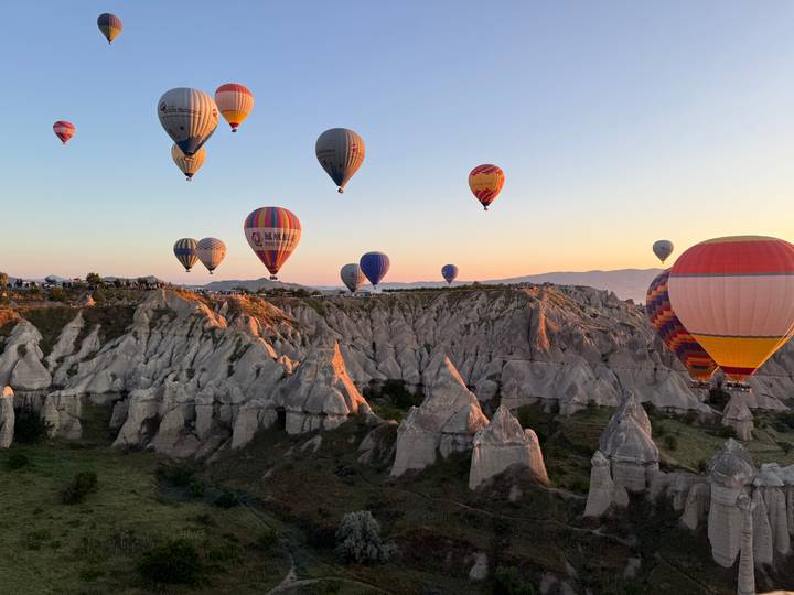 Multiple colorful hot-air balloons float over sun-lit fairy chimneys at golden hour in Cappadocia.