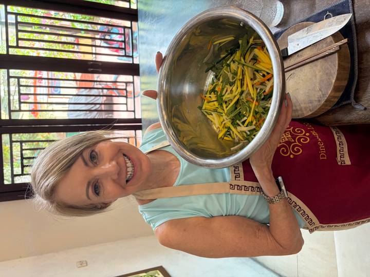 Woman proudly holds a metal bowl of freshly prepared vegetables during a Vietnamese cooking class.