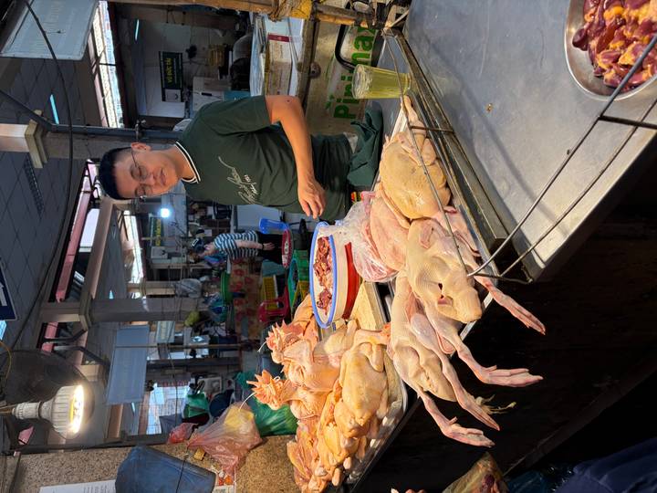 Butcher stands behind a display of plucked chickens at a traditional wet market stall.