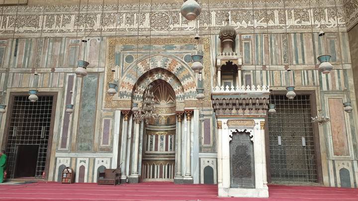 Intricately decorated entrance and red carpet of an ornate medieval mosque interior.