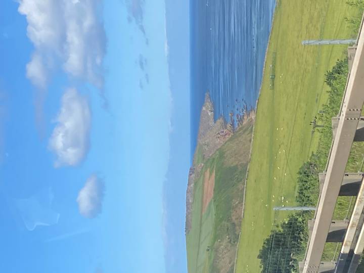 Green coastal cliffs meeting a blue sea under scattered clouds.
