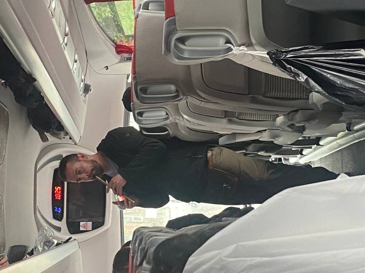 Tour guide standing in coach aisle speaking into microphone to passengers.