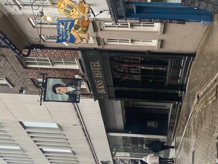 Traditional pub frontage with hanging sign reading “Burns Hotel” on a rainy street.