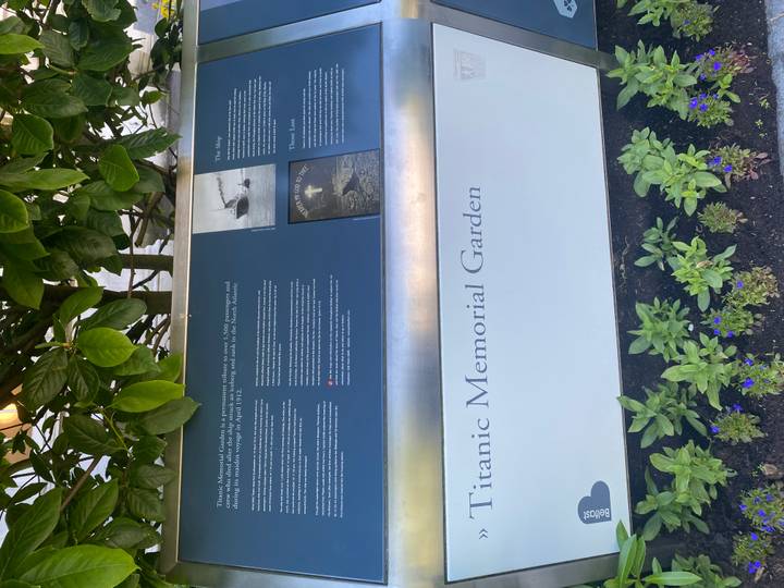 Interpretive panel for Titanic Memorial Garden surrounded by leafy plants.