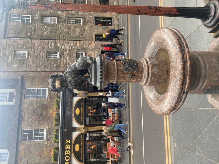 Bronze statue of Greyfriars Bobby on pedestal with busy Edinburgh street behind.