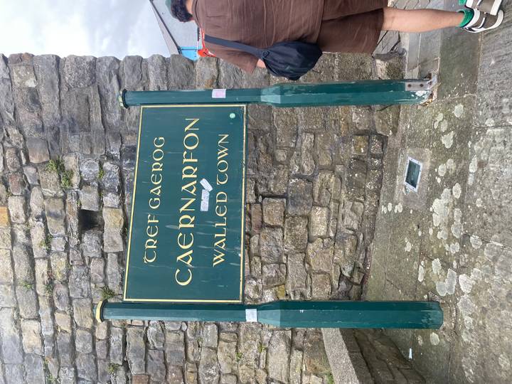Green sign marking Caernarfon Walled Town attached to stone wall.