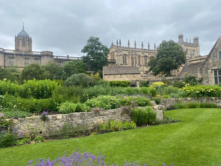 Manicured lawns and flowering borders in Christ Church College garden with historic buildings behind.