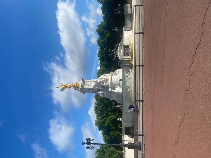 Victoria Memorial with gilded angel in front of Buckingham Palace under blue sky.