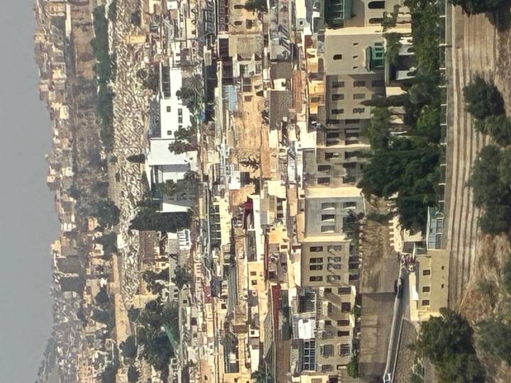 Dense hillside view of tan–colored buildings making up the old medina district of a Moroccan city under hazy midday light.