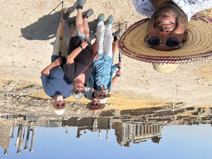Five travelers pose with trekking poles in front of sprawling Roman ruins in the Moroccan countryside.