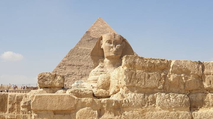 The Great Sphinx sits in front of the Pyramid of Khafre under a clear blue Egyptian sky.