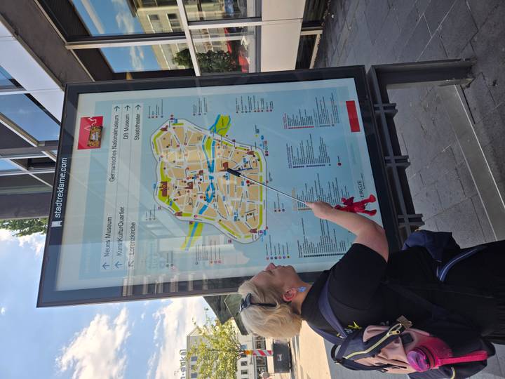Guide points at a large city tourist map displayed on a glass panel at a street corner.
