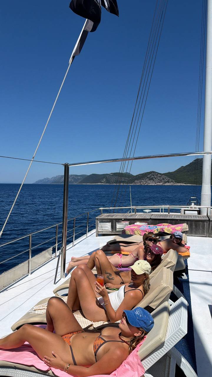 Two sunbathers relaxing on the deck of a yacht with deep blue sea and rugged Croatian coastline in the distance.