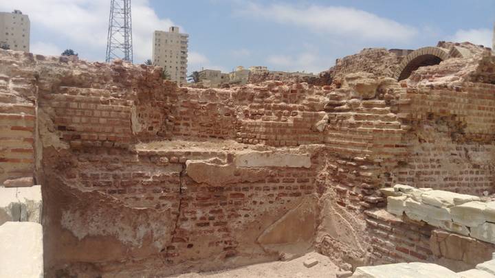 Crumbling brick and stone ruins of an ancient site with modern apartment blocks in the background.