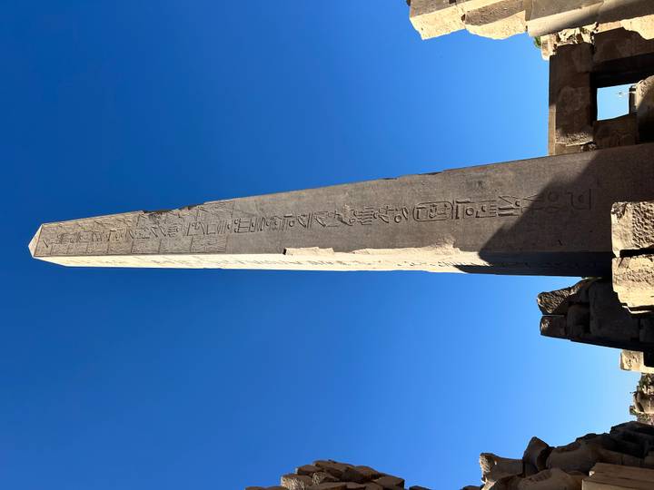 Tall ancient Egyptian obelisk with hieroglyphs reaches into vivid blue sky.