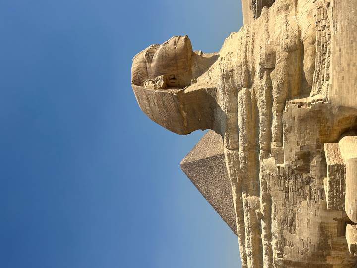 The Great Sphinx with Pyramid of Khafre rising behind under clear desert sky.