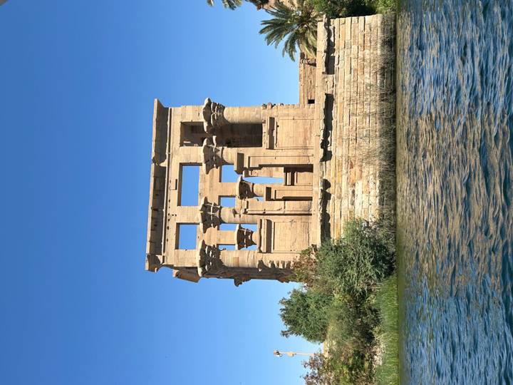 Philae Temple complex with elegant columns viewed from river level against clear sky.