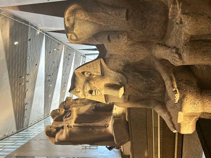Granite seated statue of an ancient pharaoh displayed inside a modern, light-filled museum hall