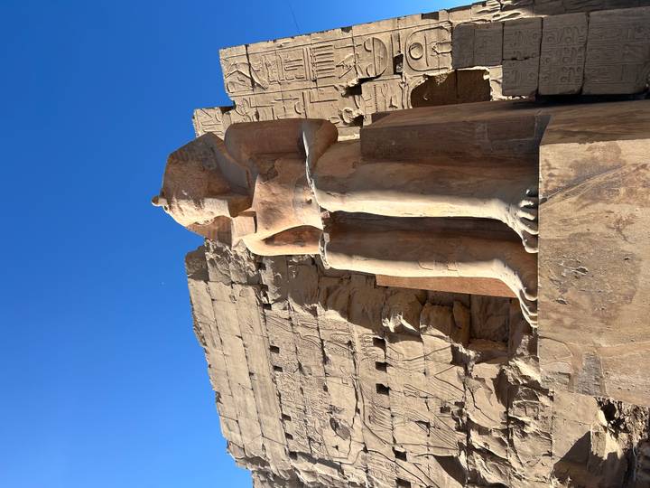 Sandstone colossus of a pharaoh seated against clear blue skies and carved temple walls