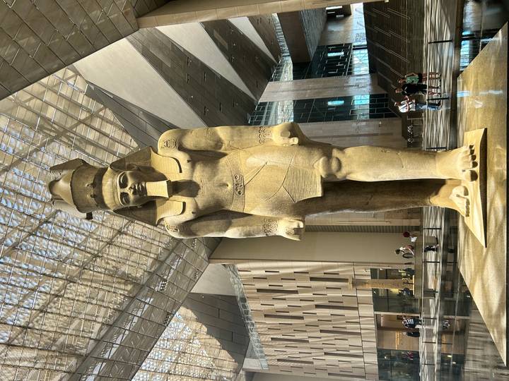Towering standing statue of Ramesses II inside a vast glass-roofed museum atrium