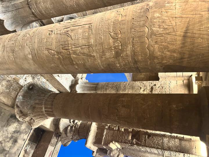 Massive sandstone columns covered in hieroglyphics inside an ancient Egyptian temple lit by warm light