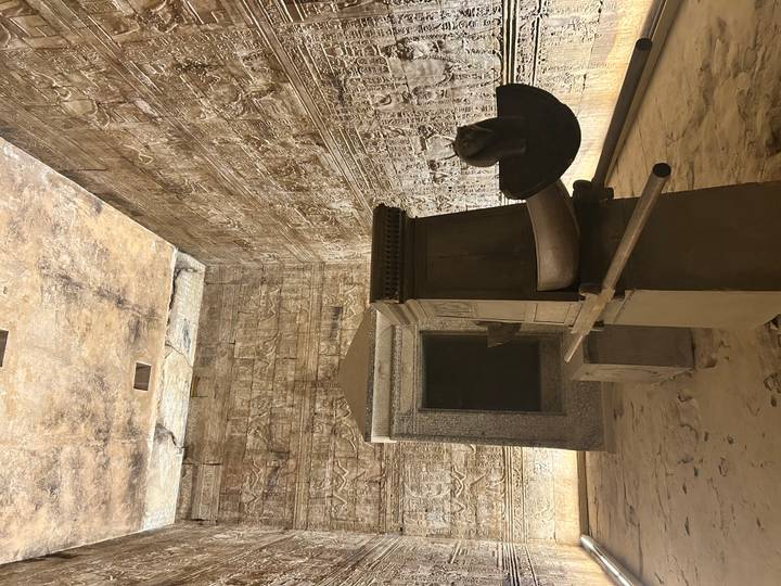 Dimly lit sanctuary chamber of an Egyptian temple featuring an ancient stone shrine and carvings