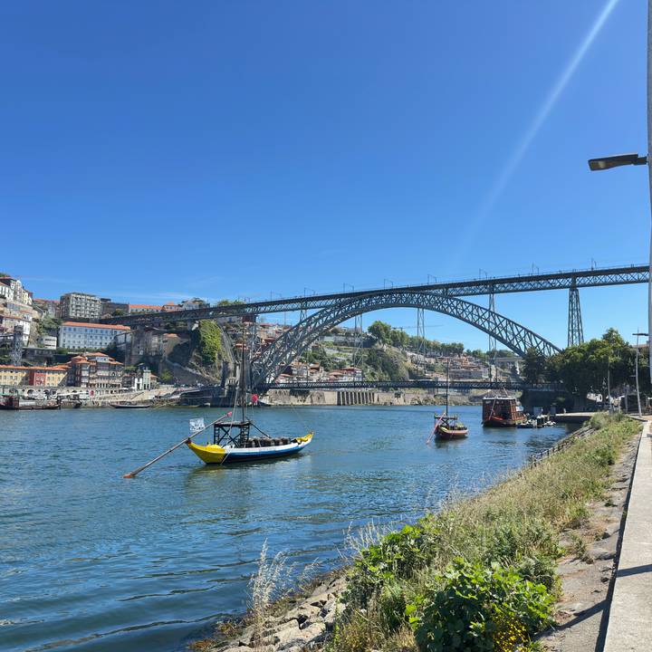 Dom Luís I Bridge spans the Douro River with traditional boats and colorful Porto hillside buildings.