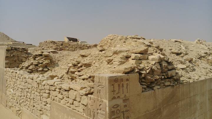 Close-up view of crumbling stone and mud-brick ruins adorned with faint hieroglyphics under hazy desert light.