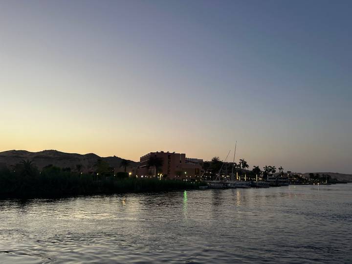 Soft evening light settles over riverside buildings and palm trees along the Nile.
