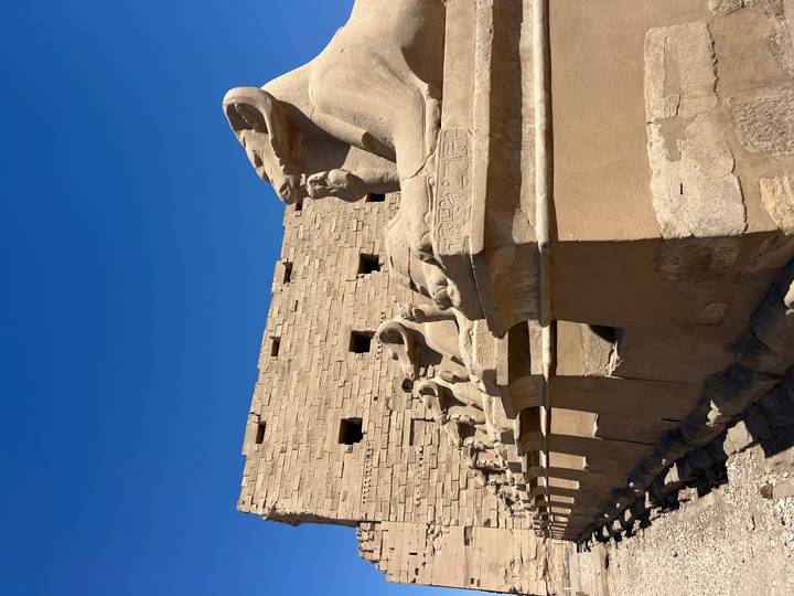 A line of ram-headed sphinx statues carved in sandstone stretches toward a tall wall at Karnak.
