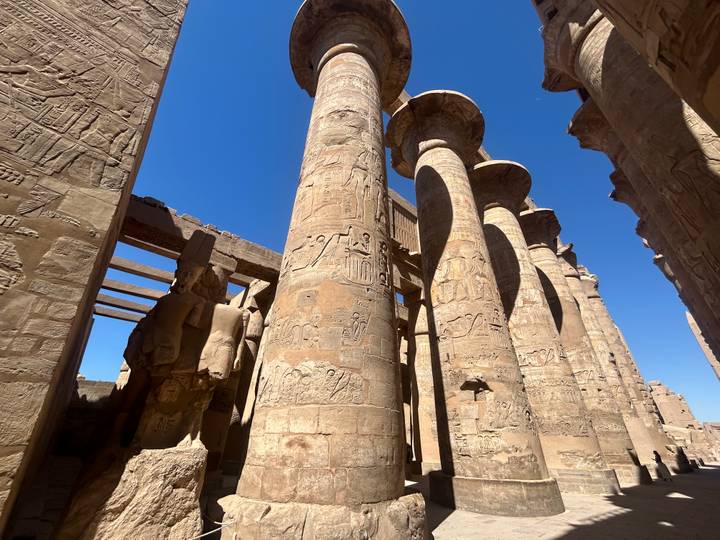 Massive ancient columns covered in hieroglyphics tower toward a vivid blue sky inside Luxor Temple.