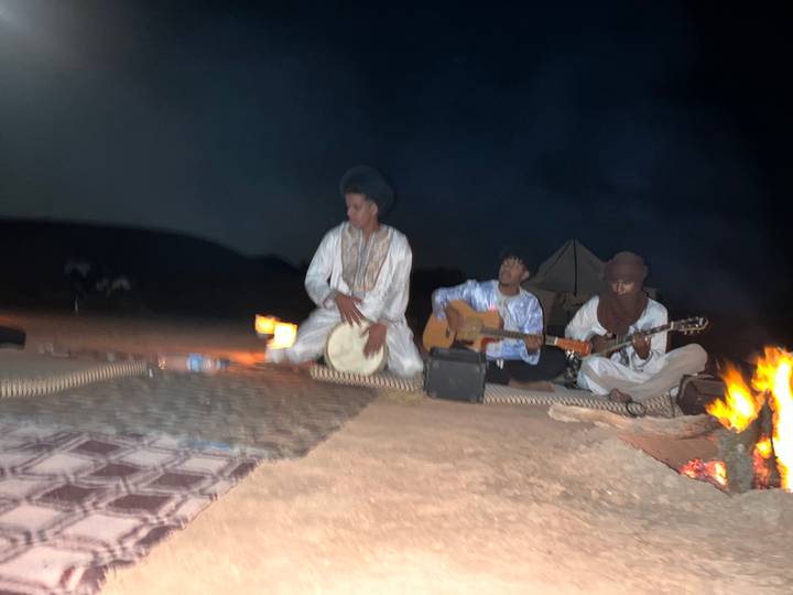Blurry night shot of three musicians performing around a small fire in the desert.