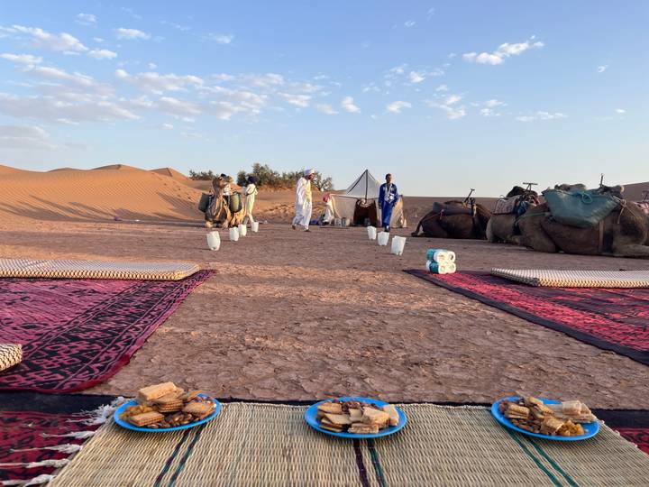 Low tables and patterned rugs await breakfast with camels and dunes in the background.